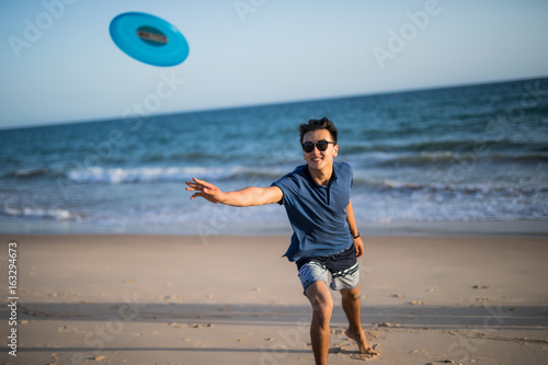 Asian manplaying frisbee  on the sea beach photo