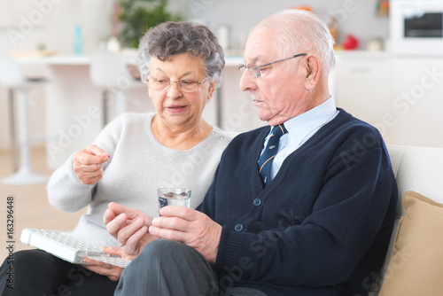 Tableau sur toile Elderly woman administering medication to husband from pillbox