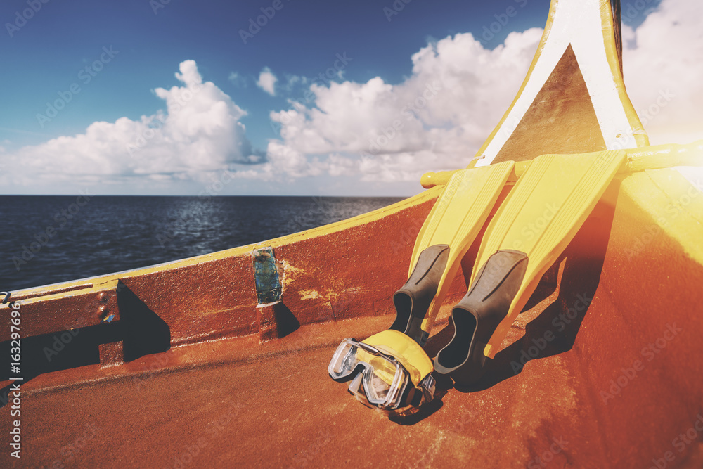 Fototapeta premium Yellow fins and swimming mask laying on bottom of diving boat next to stern on warm sunny summer day with Indian ocean in background and copy space for text, your logo or advertising message