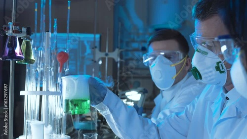 Crop group of chemists working in a laboratory conducting scientific tests using coolorful chemical solutions in assorted glassware and wearing sterility masks photo