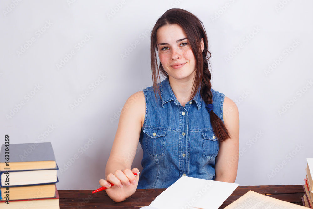 Young smiling student woman sitting at the table with empty paper sheets. Education concept Young smiling student woman sitting at the table with empty paper sheets. Education concept