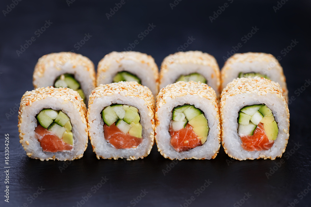Appetizing fresh california sushi roll set with salmon in sesame served on black slate, close up. Japanese healthy seafood. Appetizing fresh california sushi roll set with salmon in sesame served on black slate, close up. Japanese healthy seafood.