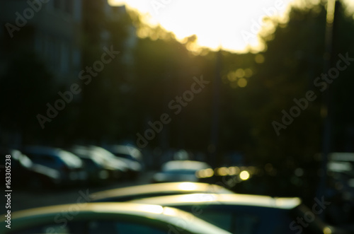 Sunset light over the trees and street in the city with roofs of parked cars. Blurred dark image.
