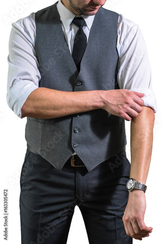 A young businessman in a white shirt rolls up his sleeves preparing to work. A guy, a hipster in a gray waistcoat with a black tie. Ready for work