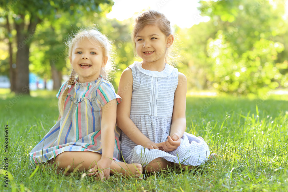 Cute little girls sitting on green grass in park Cute little girls sitting on green grass in park