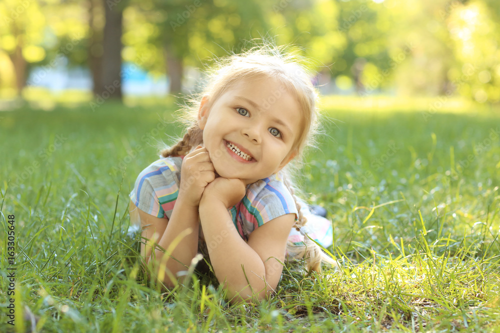 Cute little girl lying on green grass in park Cute little girl lying on green grass in park