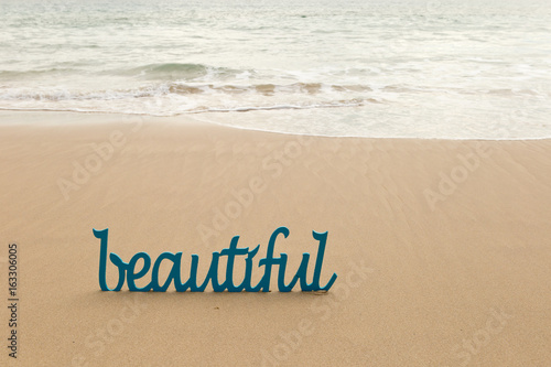 Beautiful - blue wooden word in sand with waves on beach