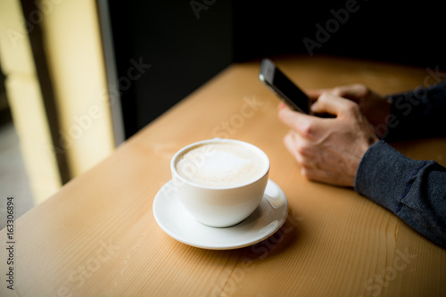 Man typing a sms on phone while drink a cup of coffee