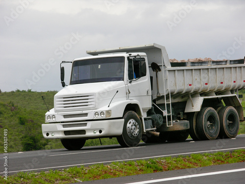 Fotografi white dump truck hauling sand going downhill