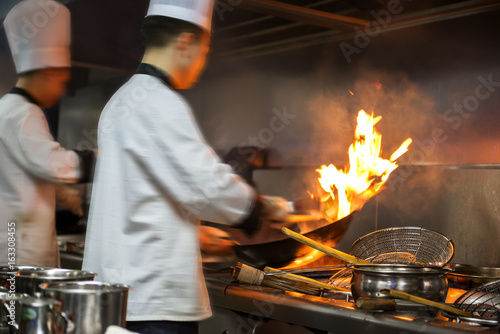 Chef in restaurant kitchen at stove with pan  doing flambe on food