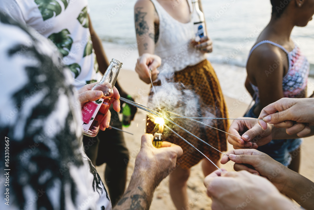 Closeup of diverse friends lighting up the sparklers by the beach