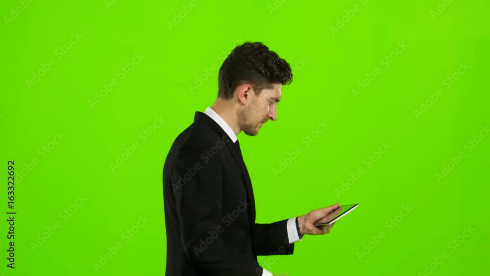 Businessman walks, thumbs a notebook, and makes a selfie. Green screen. Side view Businessman walks, thumbs a notebook, and makes a selfie. Green screen. Side view