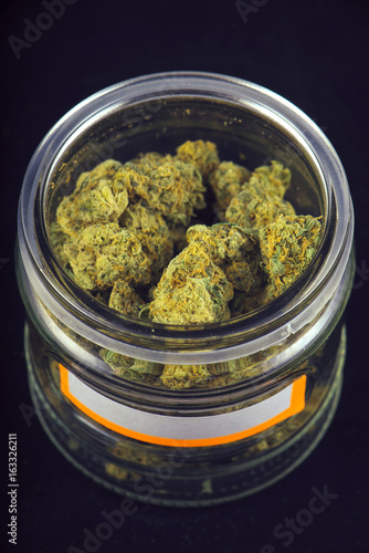 Detail of cannabis buds (grape god strain) on a glass jar isolated over black background photo