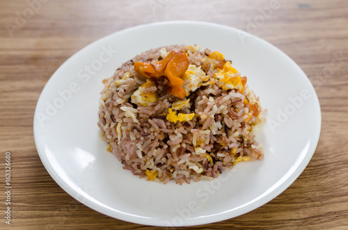 Fried brown rice with eggs and sausages on white dish.