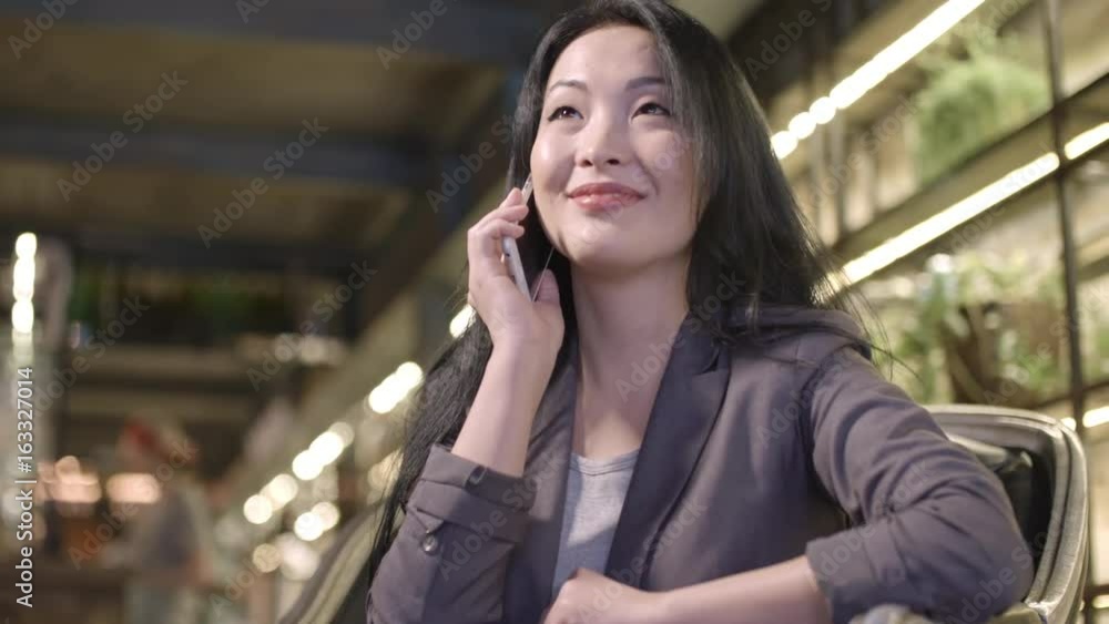 PAN of smartly dressed beautiful Asian woman dialing someone on mobile phone in cafe, then chatting and smiling PAN of smartly dressed beautiful Asian woman dialing someone on mobile phone in cafe, then chatting and smiling