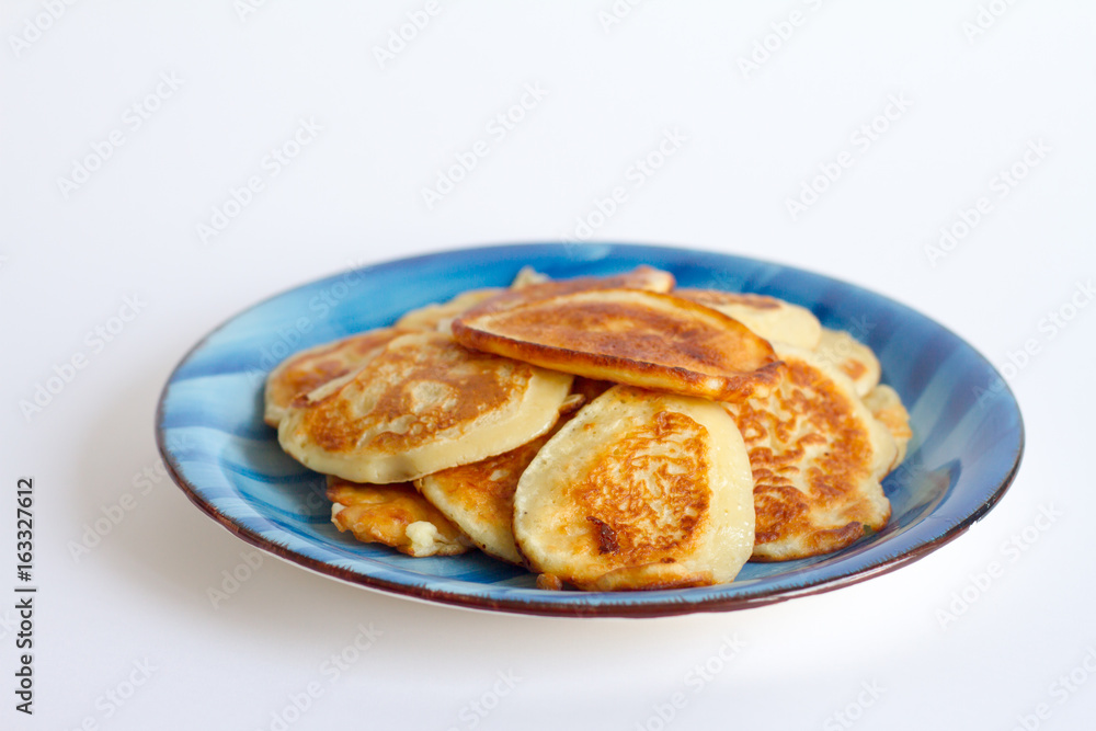 Ruddy freshly cooked pancakes lie on a blue plate on a white background.