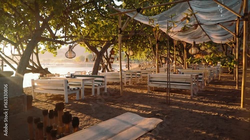 Beachside restaurant with wooden benches and tables in Pemuteran Bay, Bali on sunrise photo