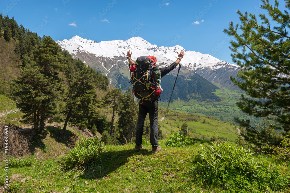 Joyful man traveler with open arms stands on the alpine meadow Joyful man traveler with open arms stands on the alpine meadow