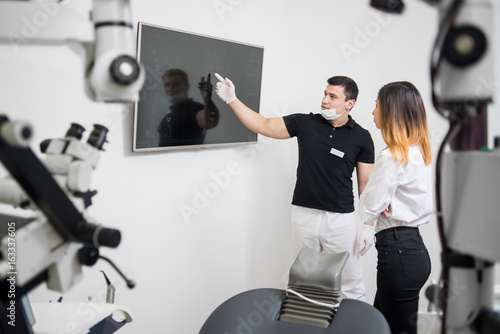 Male dentist showing to female patient her dental x-ray image on computer monitor in a dental clinic. Focus on a doctor. Dentistry