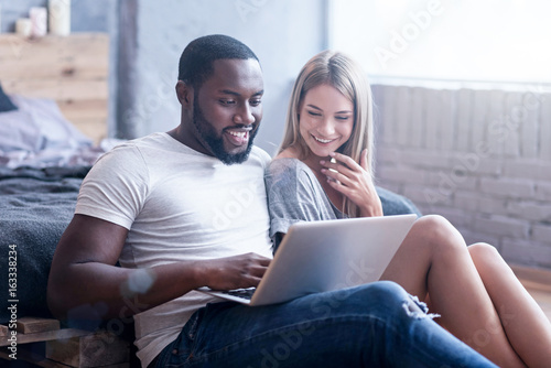 Amused international couple using laptop at home