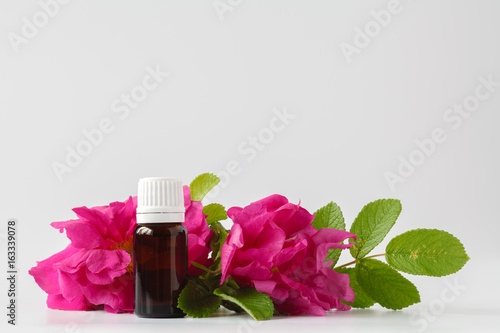 A bottle of natural wild rose oil and fresh rose flower - aromatherapy and organic skincare concept