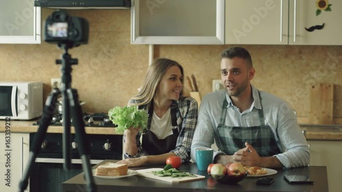 Young attractive couple shooting video food blog about cooking on dslr camera in the kitchen