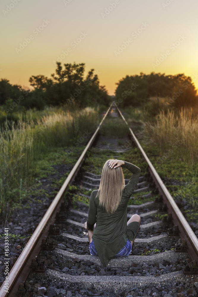 Young woman sitting on the railway at sunset Young woman sitting on the railway at sunset