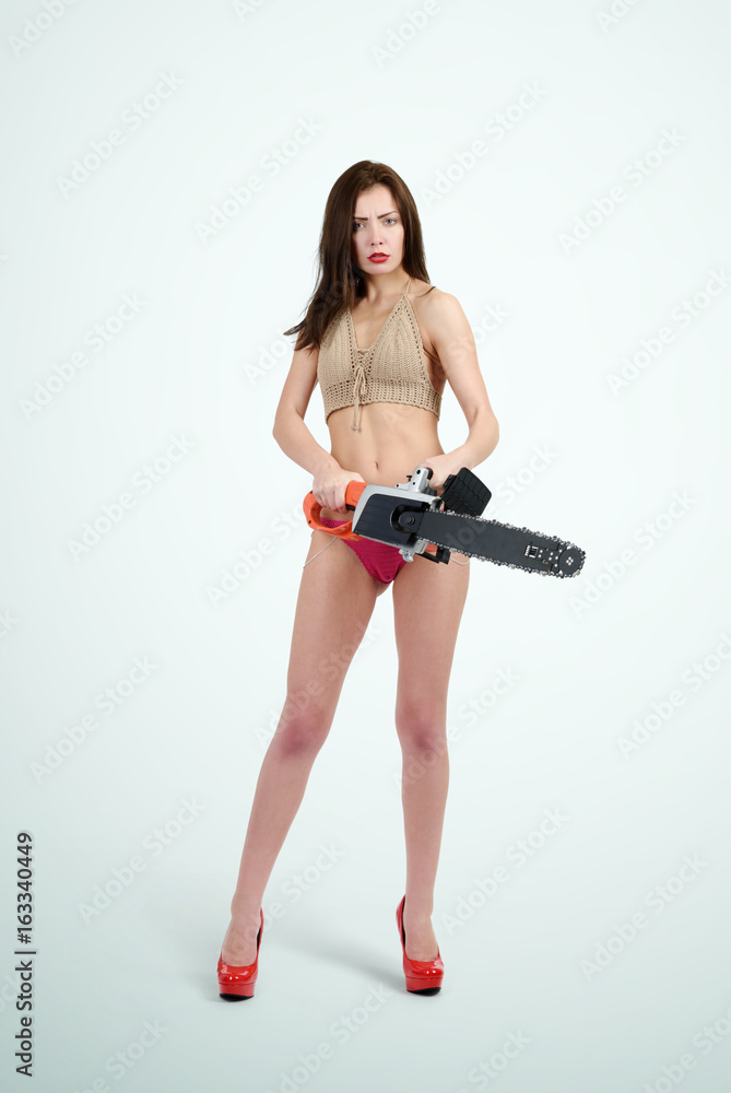 Young girl in bikini holding electric saw on background. Woman with tools concept