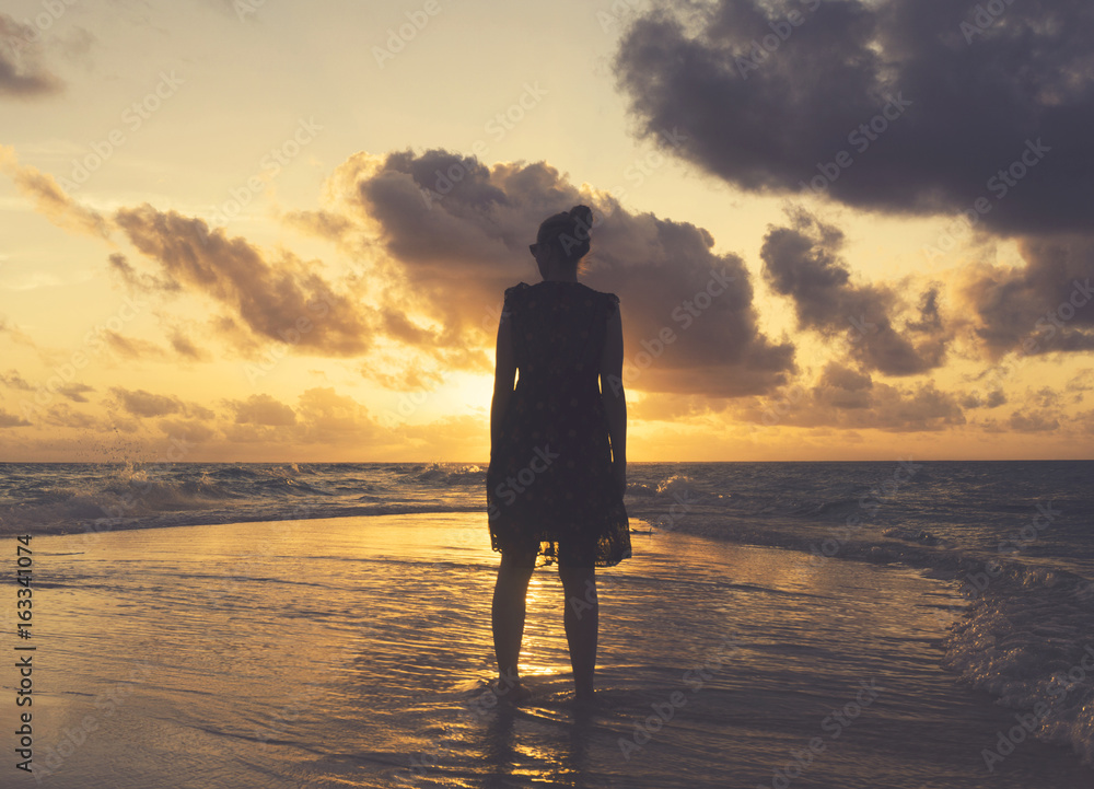 Female standing on the beach watching sunset. Travel lifestyle background