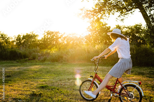 Beautiful young caucasian woman riding a bicycle in park at summer sunny day