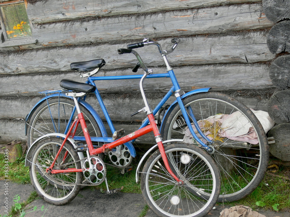 Two old bicycles of blue and red colors on the background of a wooden house
