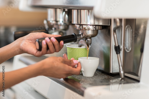 Cropped shot of female barista using coffee machine while making coffee in cafe