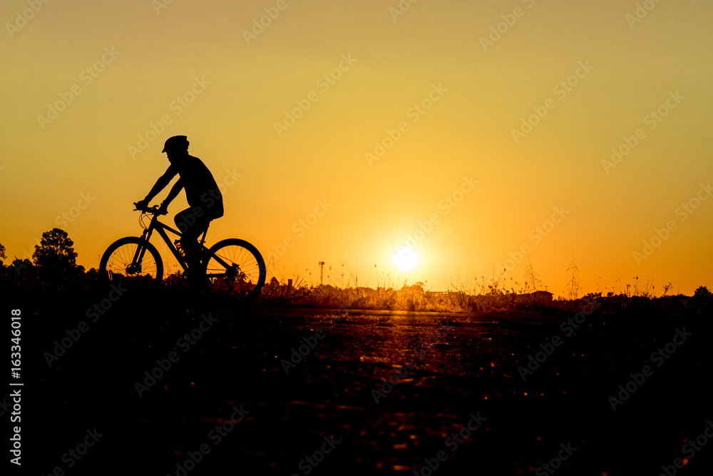 Fototapeta premium Silhouette of cyclist riding on a bike on road at sunset.