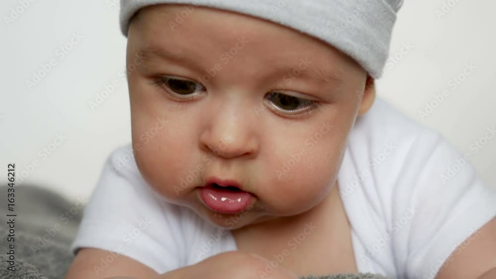 baby boy gray hat lies on her stomach and chewing on the grey towels baby boy gray hat lies on her stomach and chewing on the grey towels