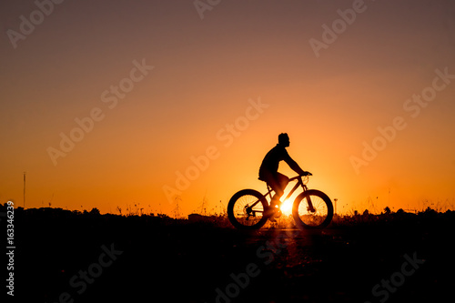 Silhouette of cyclist riding on a bike on road at sunset.