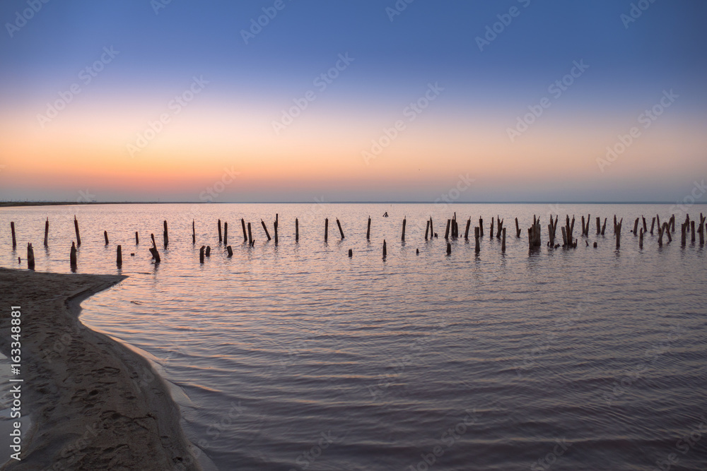 Water surface in golden glow of sunset / Abandoned destroyed wooden pier on lake at sunset