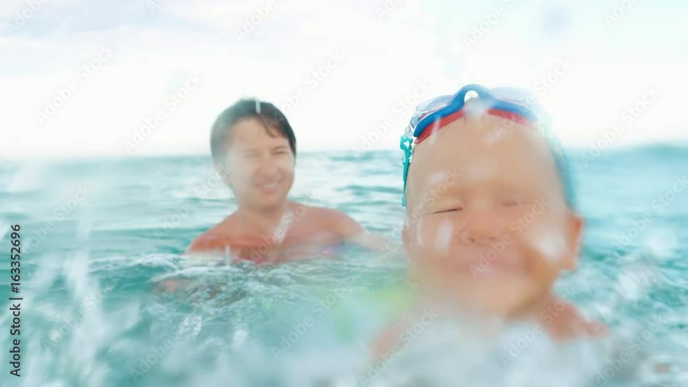 happy boy makes splash in the sea slow motion. boy in swimming goggles and his mother having fun in the sea happy boy makes splash in the sea slow motion. boy in swimming goggles and his mother having fun in the sea