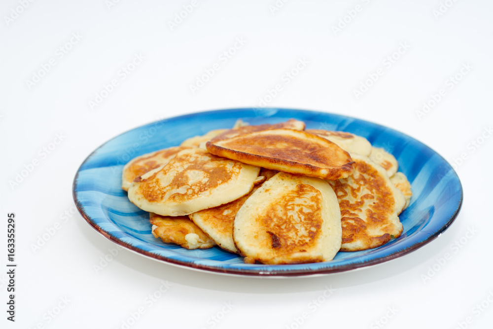 Ruddy freshly cooked pancakes lie on a blue plate on a white background.