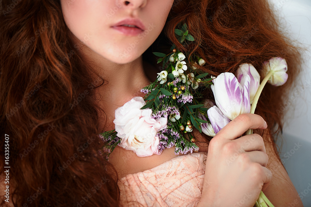 Naklejka premium Beautiful romantic red-haired girl sitting in the bath and holding flowers .part of the face is not visible. In lace dress powdery pastel cream color