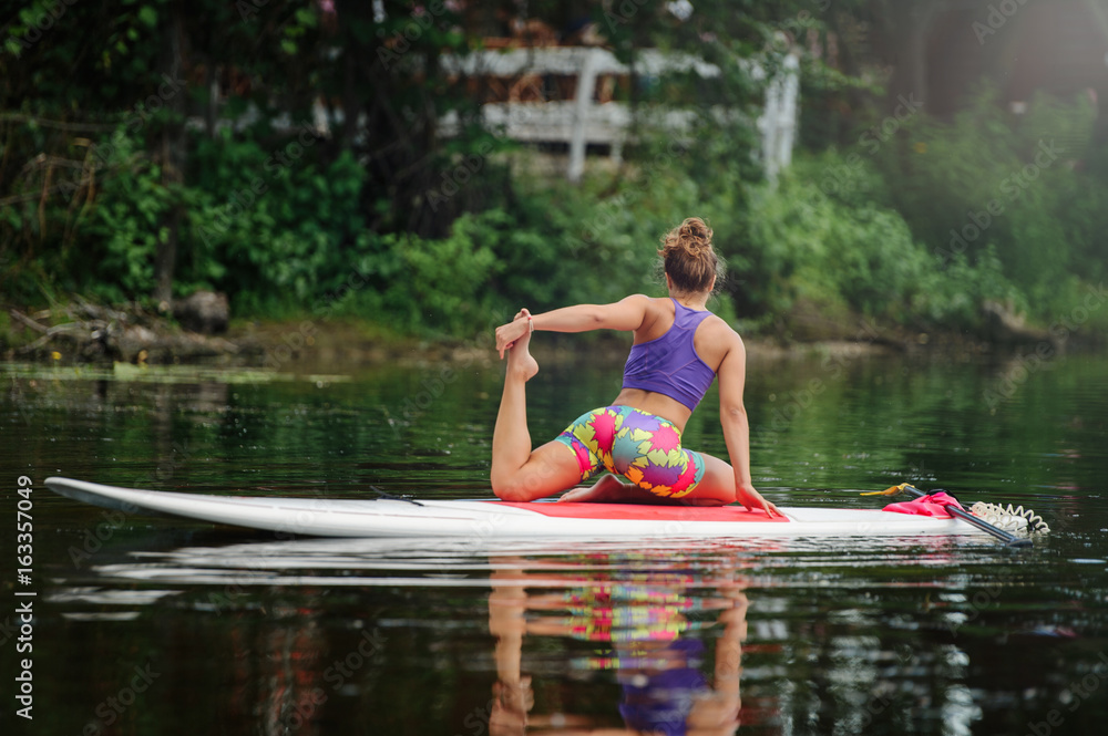 Fototapeta premium Young woman doing fitness on a board with an oar. Side view - the concept of harmony with nature, a free and healthy lifestyle, supernumerary staff