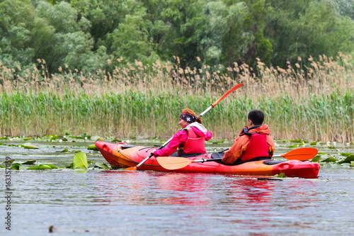 Couple man and woman - family kayaking in wild lake among thickets of plants on biosphere reserve in spring. Fun together enjoying adventurous experience with kayak during vacation