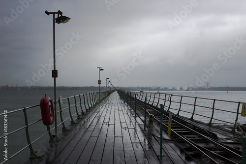 The long pier at Hythe in the south of England with its wooden walkway and railway line to the Southampton Ferry that leaves from the pier. Pictured on a dull wet overcast day in June