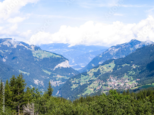 Landscape view of Swiss alps snow covered mountains and green hills with city, town or village in Lugano, Ticino canton