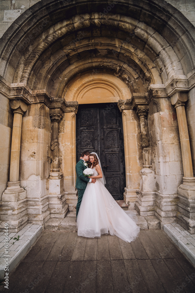 Fototapeta premium Happy newlywed couple portrait, face closeup of newlywed blonde bride hugging smiling groom near old metal gate, emotional couple on honeymoon