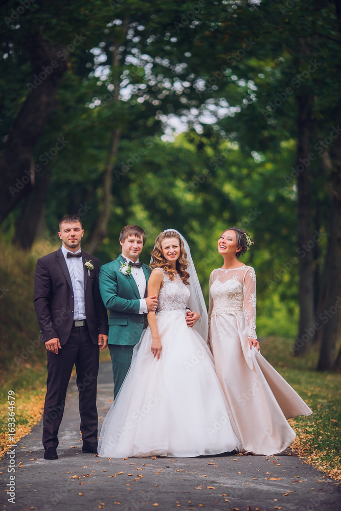 Portrait of newlywed couple having fun with bridesmaids and groomsmen in green sunny park