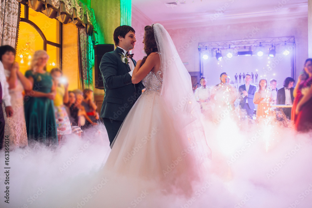 Beautiful caucasian couple just married and dancing their first dance confetti and heavy smoke around. Bride and groom kiss.