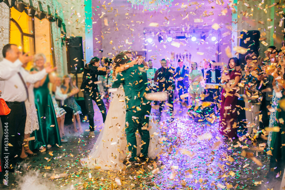 Beautiful caucasian couple just married and dancing their first dance confetti and heavy smoke around. Bride and groom kiss.