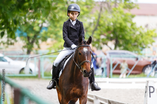 Young teenage girl in helmet riding horse on dressage equestrian competition