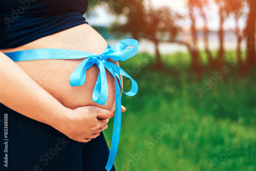 Pregnant woman outdoor with present riband on abdomen photo