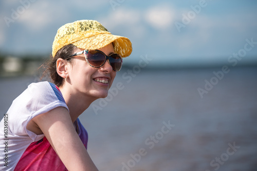 Happy girl in a baseball cap and sunglasses smiling against a sea beach background © kulkann